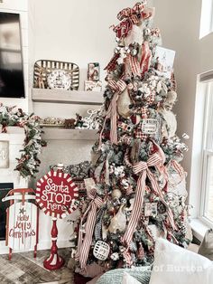 a christmas tree decorated with red, white and silver ribbons is in the corner of a living room