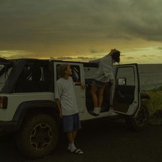 two people standing on the back of a white jeep with their feet in the open door