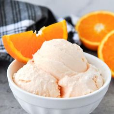 an orange ice cream in a white bowl next to sliced oranges on a table