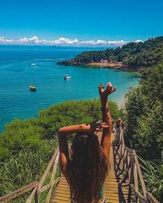 a woman standing on top of a wooden bridge next to the ocean with boats in the water