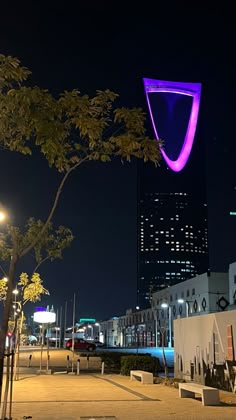 the building is lit up with purple lights at night in front of trees and benches