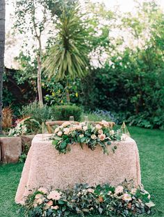 a table with flowers and greenery on it in the middle of a lawn area