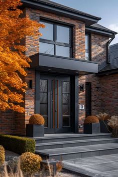 a modern house with black front doors and steps leading up to the entry door, surrounded by autumn foliage