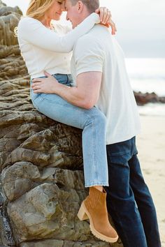 a man and woman are hugging on the rocks at the beach by the water's edge