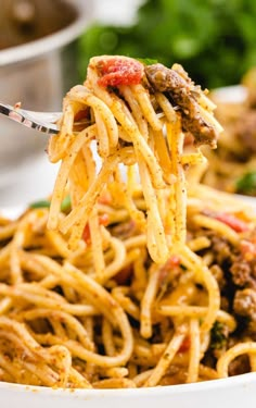 a fork full of spaghetti being lifted from a white bowl with meat and vegetables in the background