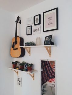 a guitar is hanging on the wall next to some shelves with pictures and other items