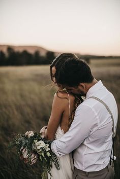 a bride and groom embracing in a field