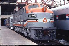 an orange and grey train is parked at the station next to another blue and gray train