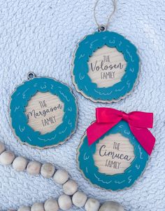 three wooden ornaments with the names of two families on them and a pink ribbon tied around one ornament