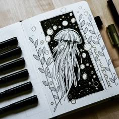 an open notebook with some pens on top of it and a drawing of a jelly fish