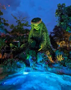 a large green monster statue sitting on top of a rock next to a blue pool