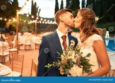 a bride and groom kissing in front of an outdoor dinner table with lights on the background