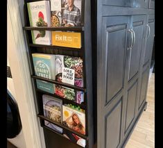 a book shelf in the corner of a kitchen with books on it and magazines hanging from them