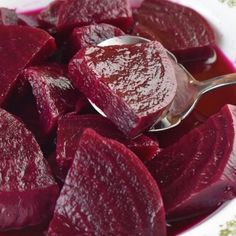 a white bowl filled with beets on top of a wooden table next to a spoon