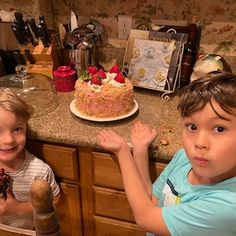 two young boys standing in front of a cake on a counter top next to each other