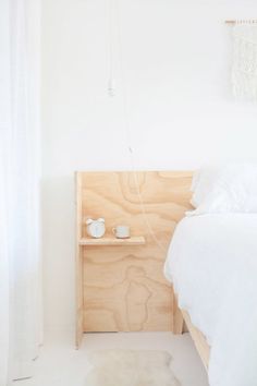 a bed with white sheets and pillows in a bedroom next to a wooden headboard