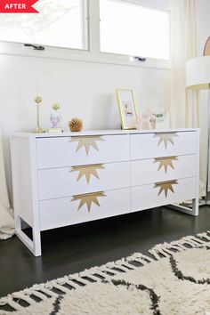 a white and gold dresser in a room with two windows, rugs and pictures on the wall