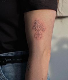 a woman with a tattoo on her arm holding a glass vase filled with daisies