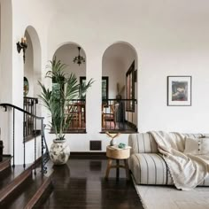 a living room filled with furniture next to a stair case and potted plant on top of a wooden table