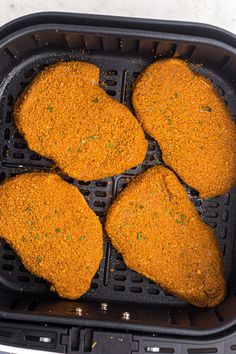 four pieces of fried chicken in a black air fryer with seasoning sprinkles