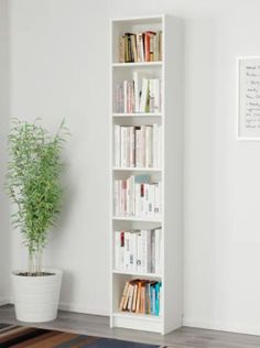 a white book shelf with books on it in a room next to a potted plant