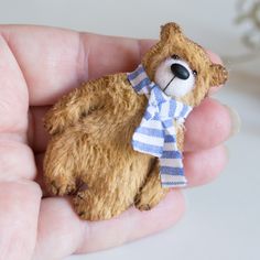 a small teddy bear wearing a blue and white striped shirt is held in someone's hand