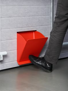 a person standing next to a red object on the floor in front of a wall