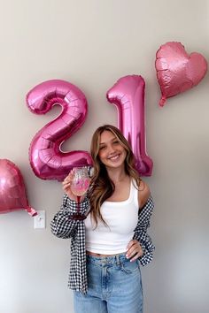 a woman standing in front of pink balloons and the number twenty two, holding a cupcake