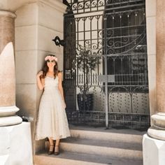 a woman in a white dress is standing on the steps outside an iron gate with a pink flower in her hair