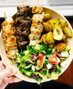 a person holding up a bowl filled with meat and veggie skewers