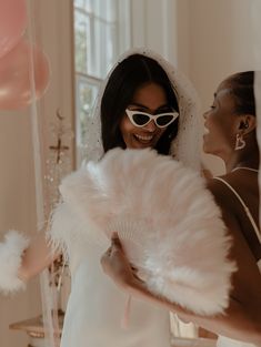 two women dressed in white are smiling at each other while one holds a large fan