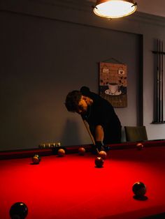 a man leaning over a pool table to pick up some balls in the dark room