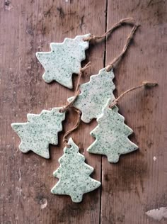 four ceramic christmas tree ornaments hanging from twine on wooden planks, with string