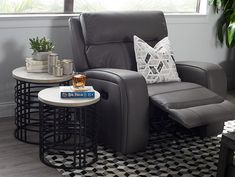 a grey recliner chair sitting next to a table with a book on top of it