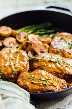 a skillet filled with meat covered in gravy next to asparagus