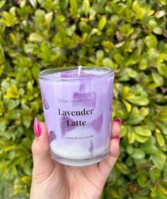 a hand holding a candle in front of some bushes and plants with the words lavender latte written on it