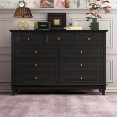 a black dresser with gold knobs and flowers on the wall above it is in a room