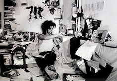 a black and white photo of a person sitting in a messy room