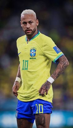 a man with tattoos on his arms and legs wearing a yellow soccer jersey standing in front of the camera