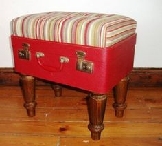 a red suitcase sitting on top of a wooden floor next to a white and brown striped seat