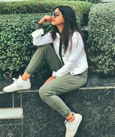 a woman sitting on the steps with her hand in her mouth and wearing white sneakers