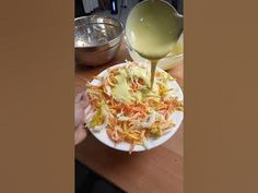 a person pouring dressing onto a plate with coleslaw and carrots on it