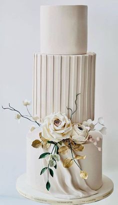 a three tiered wedding cake with white flowers on the top and gold leaf decoration