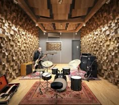 two men are playing drums in a room with wood paneling on the walls and floor