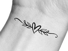 a small heart tattoo on the wrist is shown in black and white ink, with an arrow