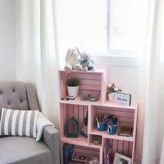 a living room with a gray couch and pink shelving unit in front of a window