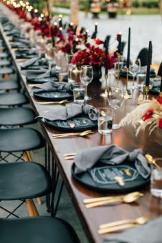 a long table set with black plates and place settings for an outdoor dinner party by the water