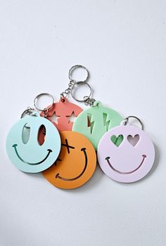 four different colored smiley face keychains on a white surface with one smiling and the other frowning