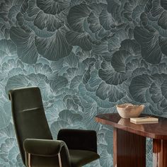 a green chair sitting next to a wooden table in front of a wall with flowers on it