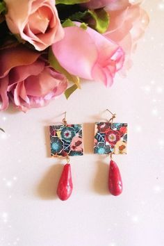 a pair of red earrings sitting on top of a white table next to pink flowers